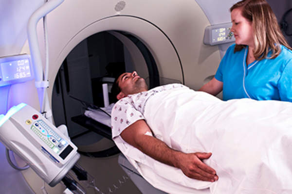 Man entering MRI machine overseen by nurse.