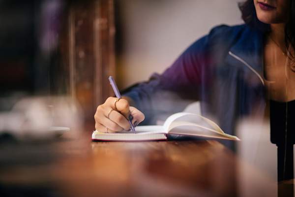Woman writing in her journal at coffee table.