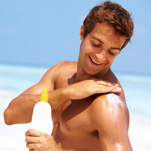 Young man putting suntan lotion on his shoulder.