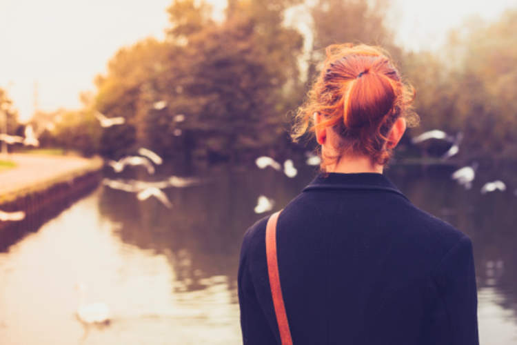 A woman looks at birds in a pond.