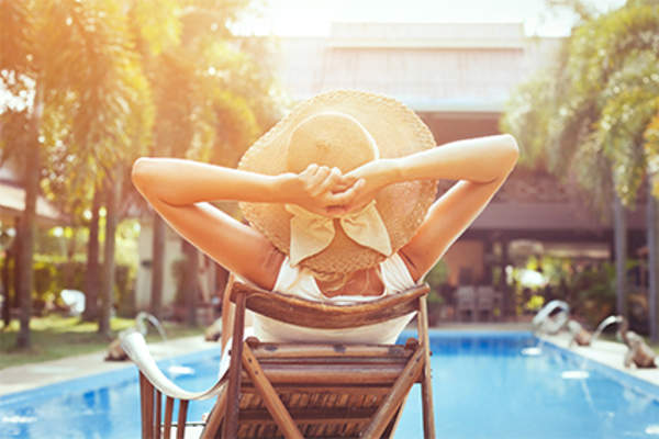 Woman in sun hat relaxing on vacation by the pool.