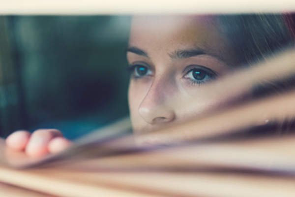 Scared woman peeking through the blinds.
