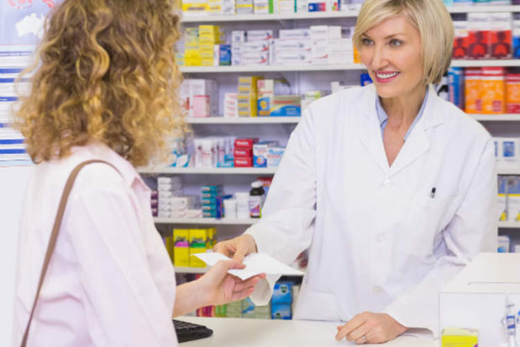 Customer handing a prescription to smiling pharmacist