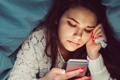 Crying girl in bed texting on smartphone