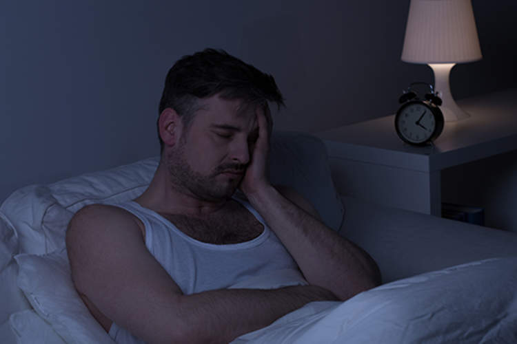 Man sitting in bed at night with a headache.