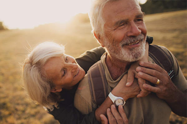 Senior couple smiling and embracing outside in sunshine.