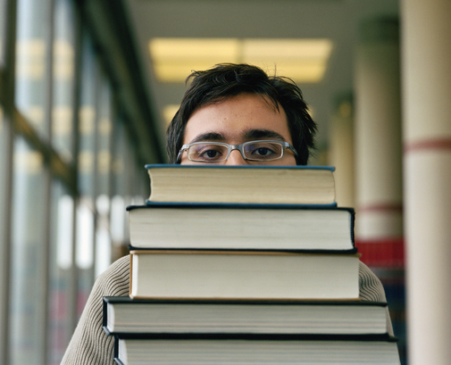 Young man carrying stack of books, close-up, portrait