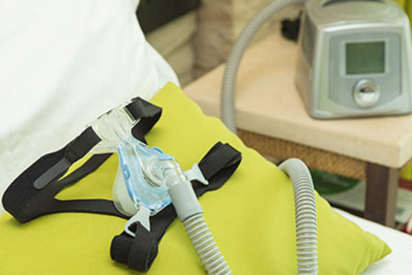 CPAP headgear mask with air tube and machine in bedroom.