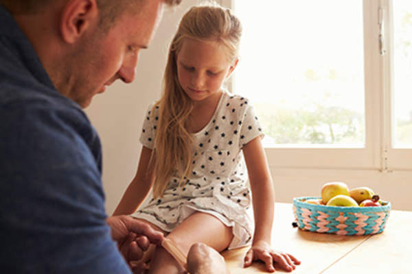 Dad putting a bandaid on his daughter's knee.