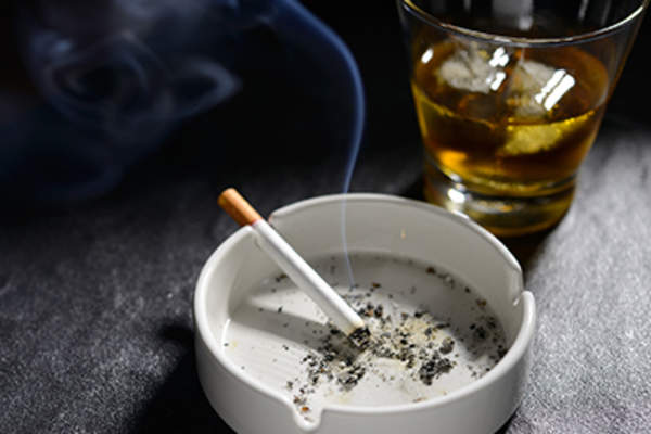 Lit and smoking cigarette in ashtray with glass of whiskey.