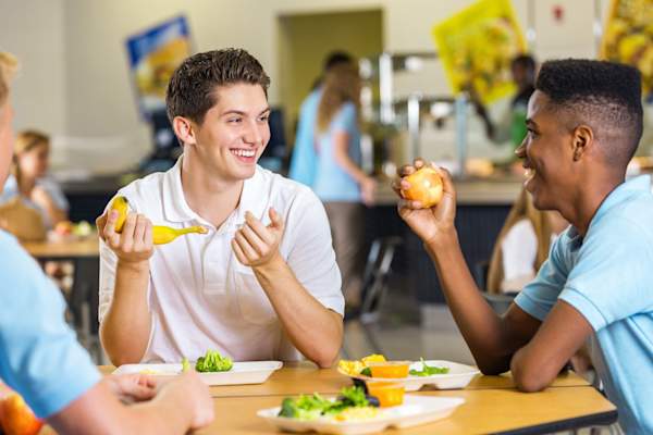 High school boys laughing together while eating lunch in cafeteria.