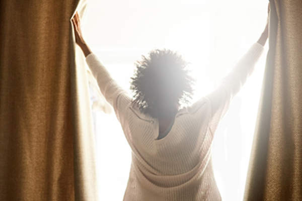 Woman opening the curtains and letting light inside.