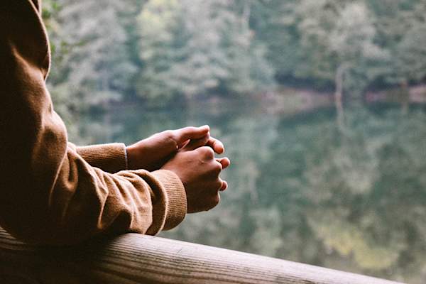 Person in brown jacket with hands folded, contemplating