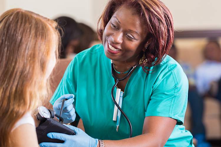 Smiling nurse taking teen girl's blood pressure.