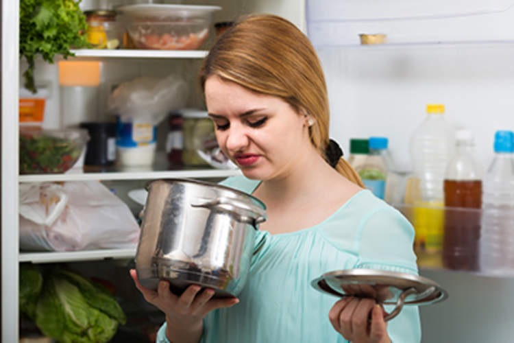 Young woman smelling spoiled food in pan.