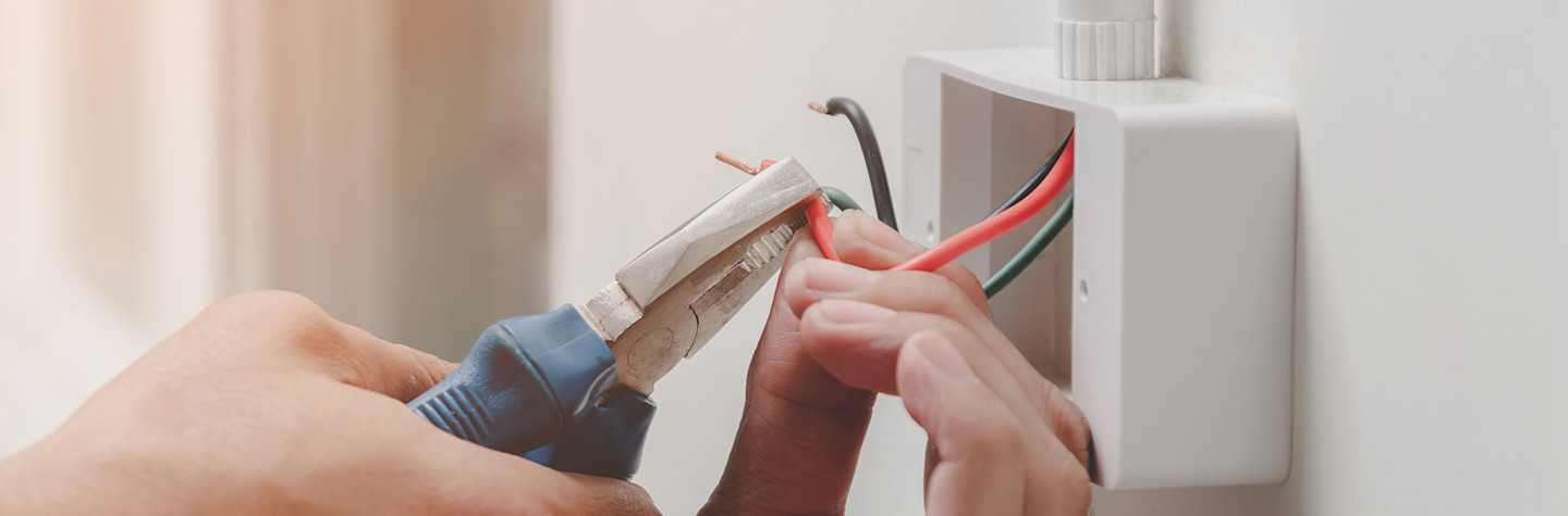 Close-up van handen die met een combinatietang een draad van een stopcontact doorknippen