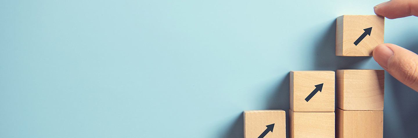 Close-up van een hand die houten blokken opstapelt op een achtergrond van lichtblauw papier