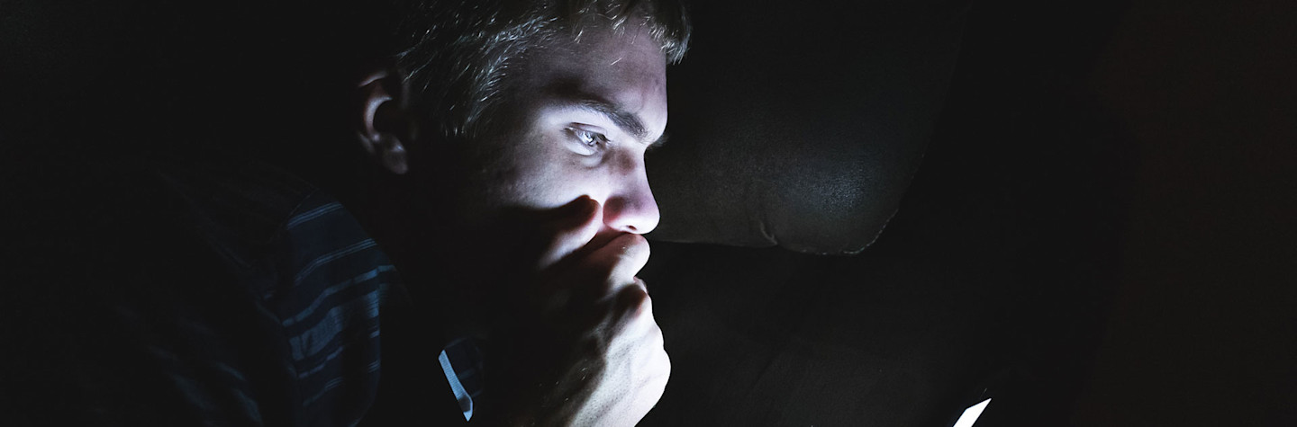 Tiener die in een donkere kamer zit en schokkend nieuws leest op zijn smartphone