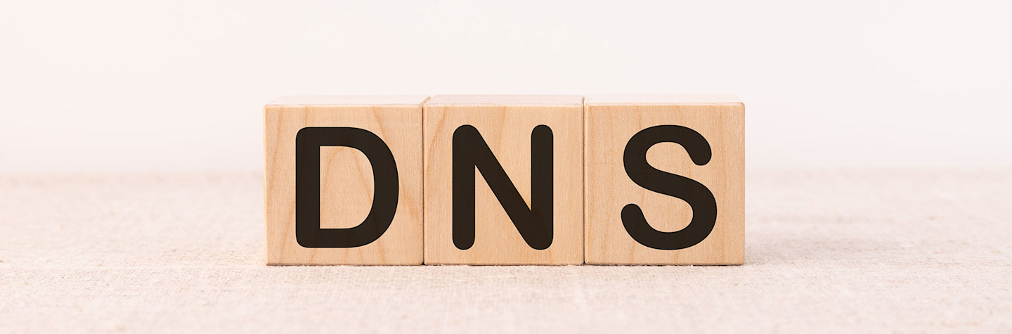 De letters 'DNS' (Domain Name System) op lichtgekleurde houten blokken tegen een lichte achtergrond.