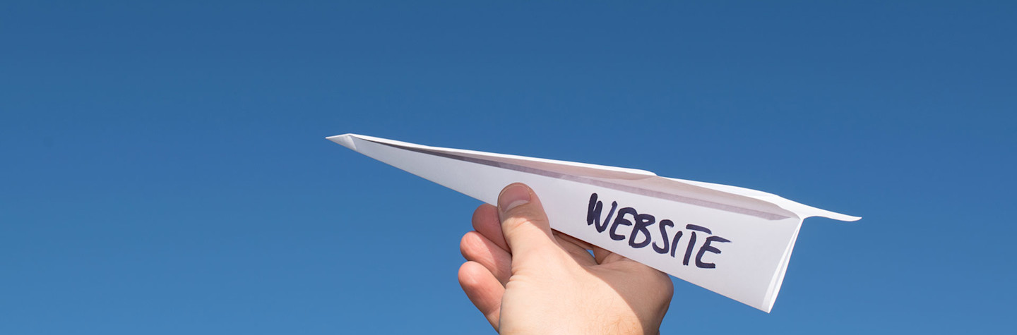 Papieren vliegtuigje met de tekst 'website' in een hand tegen een blauwe lucht. (Concept van de lancering van een website. )