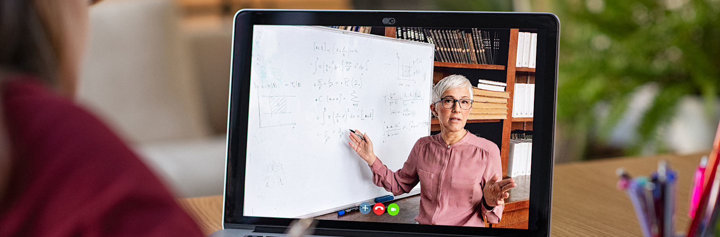 Jonge vrouw maakt aantekeningen terwijl ze naar het computerscherm kijkt en een wiskundeles volgt.