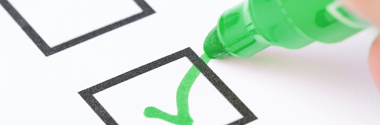 Macro shot of a hand placing a green check mark in the checklist box