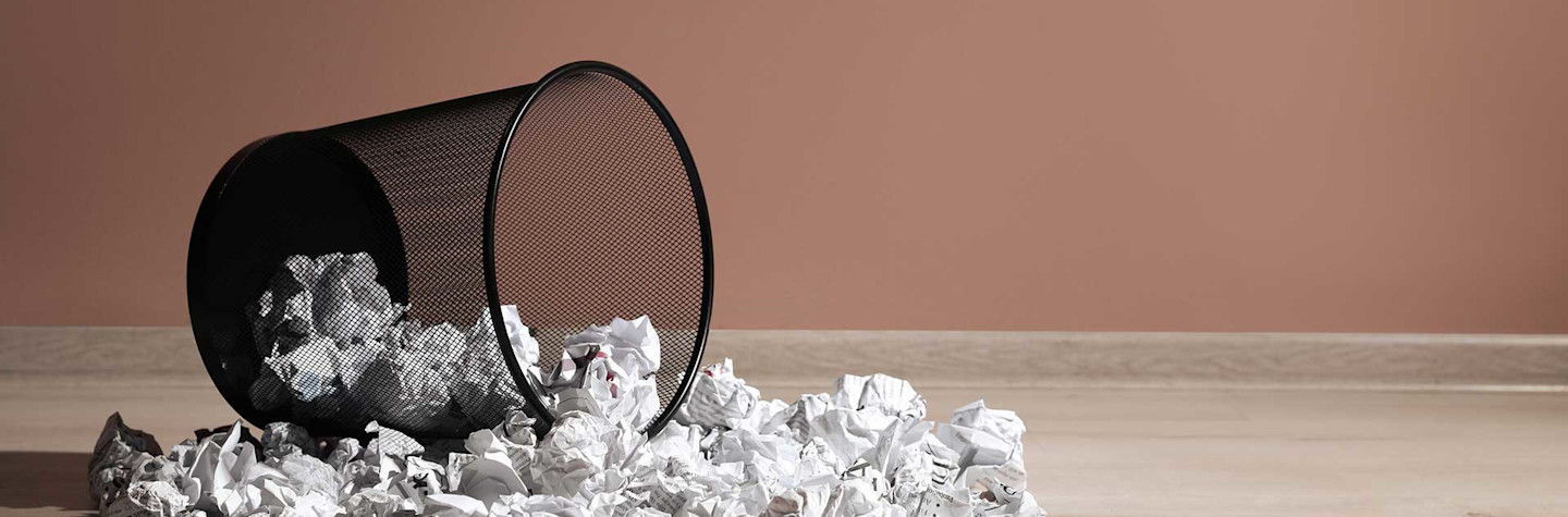 Overturned trash can with wads of paper scattered on the ground around it
