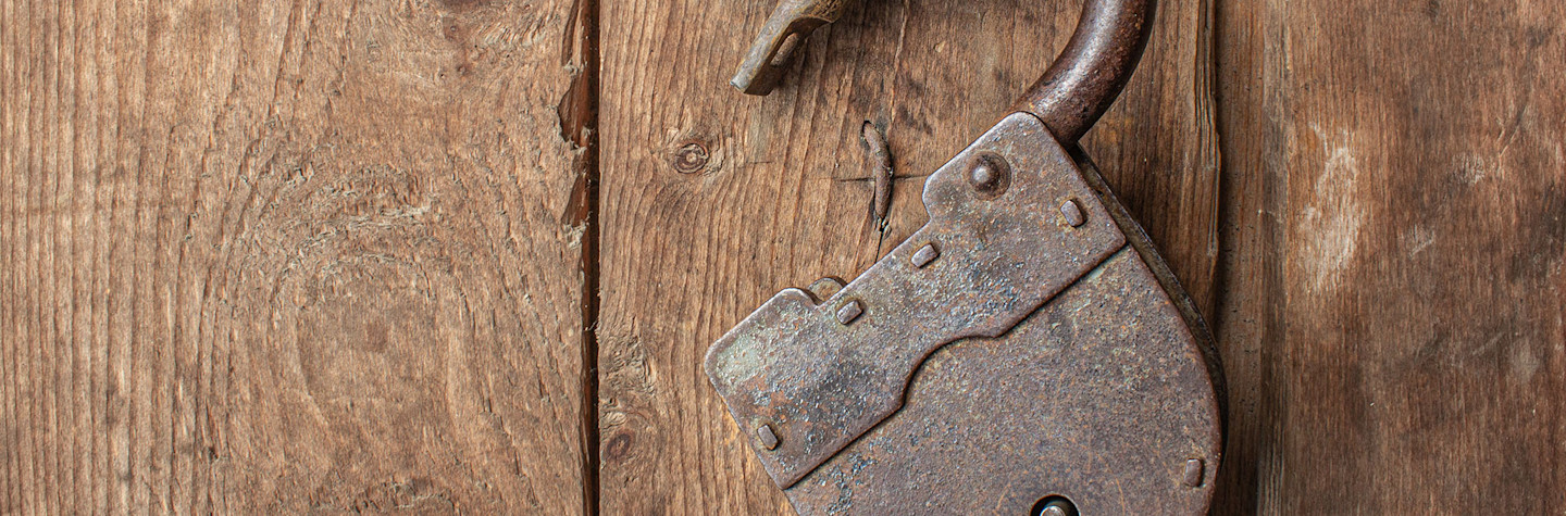 Oud, roestig, geopend hangslot zonder sleutel hangend aan een houten deur