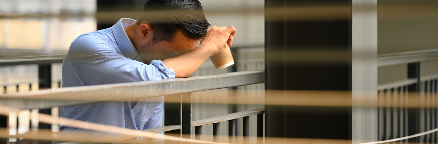 Office worker leans worriedly against a railing.