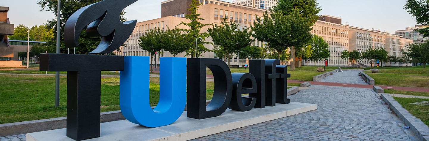 Uitzicht op de campus van de Technische Universiteit Delft, Nederland met het logo van de universiteit in levengrote letters op de voorgrond.