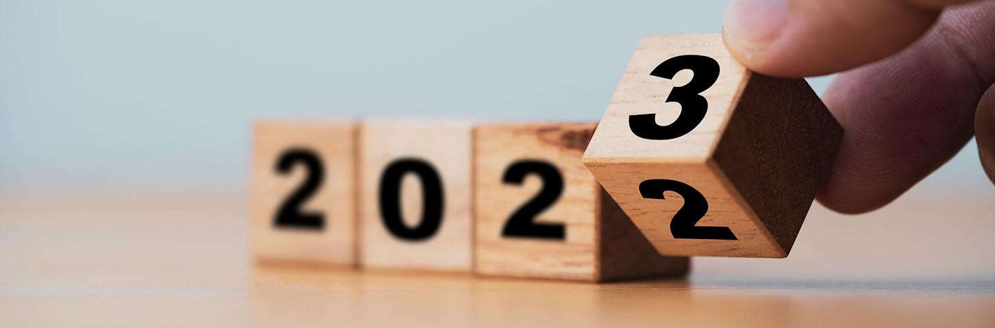 Hand flipping a wooden block from 2 to 3, so that the year 2023 is visible.