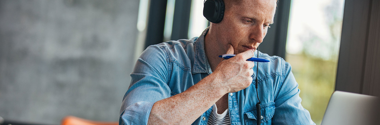 Pensive student with headphones on studying behind a laptop