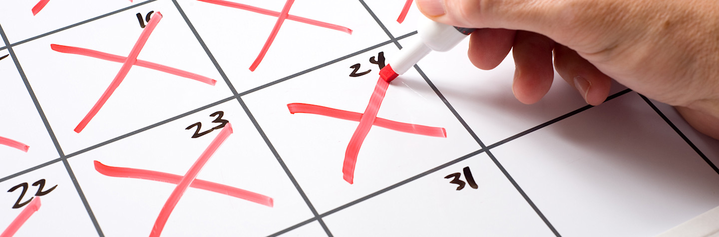 Hand met een marker die dagen afkruist op een kalender.