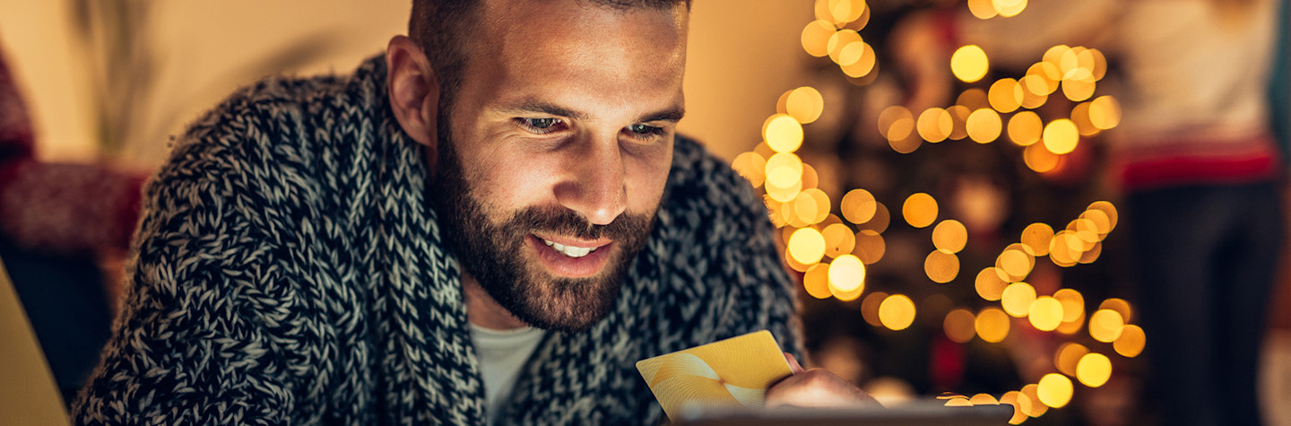 Man met creditcard in de hand doet kerstinkopen op een tablet