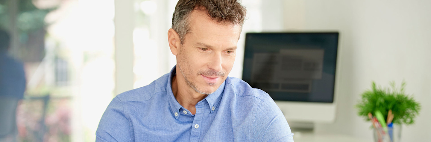 Man sitting behind a desk looks at a laptop screen.