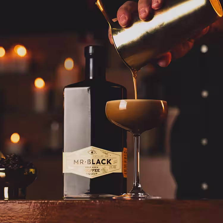 A person straining the espresso martini cocktail into a martini glass.