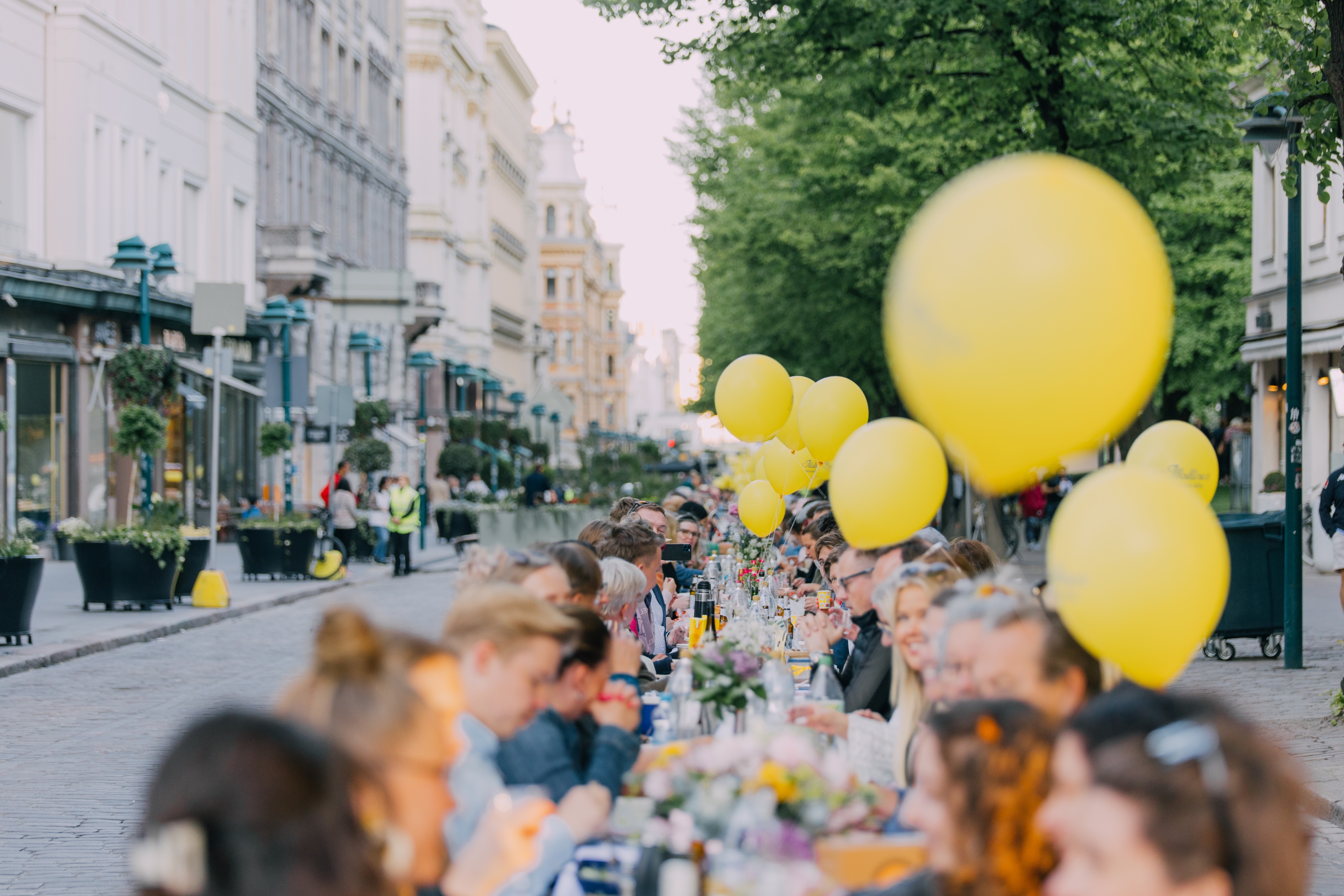 Ihmisiä ruokailemassa pitkän pöydän äärellä Helsingin keskustassa.