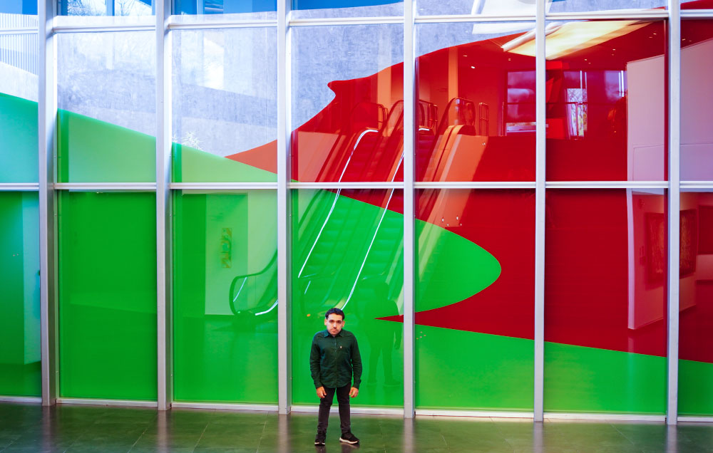 Imagen de Elian Chali junto a la obra Horizonte cancelado, una pintura mural sobre el ventanal del subsuelo de Casa Naranja.