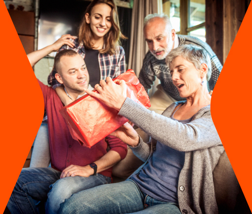 Familia al rededor de mamá en su día, viendo cómo abre su regalo.