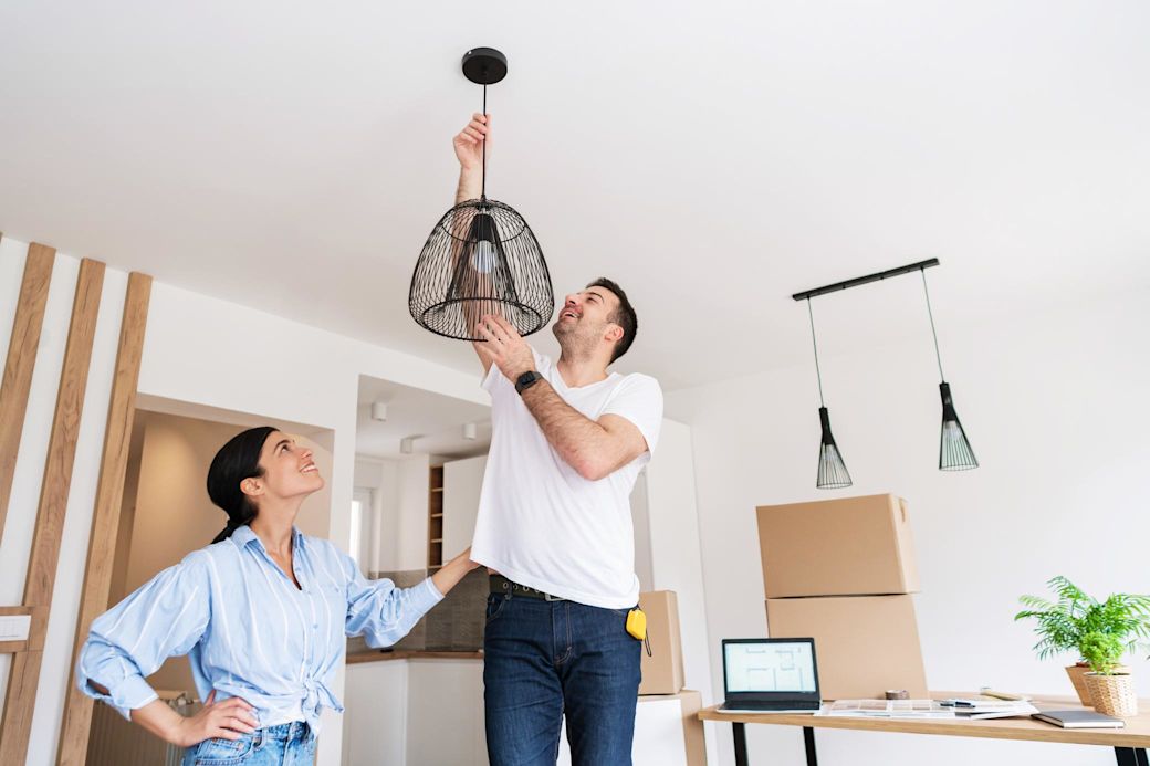 Junges Paar hängt Lampe im Wohnzimmer auf