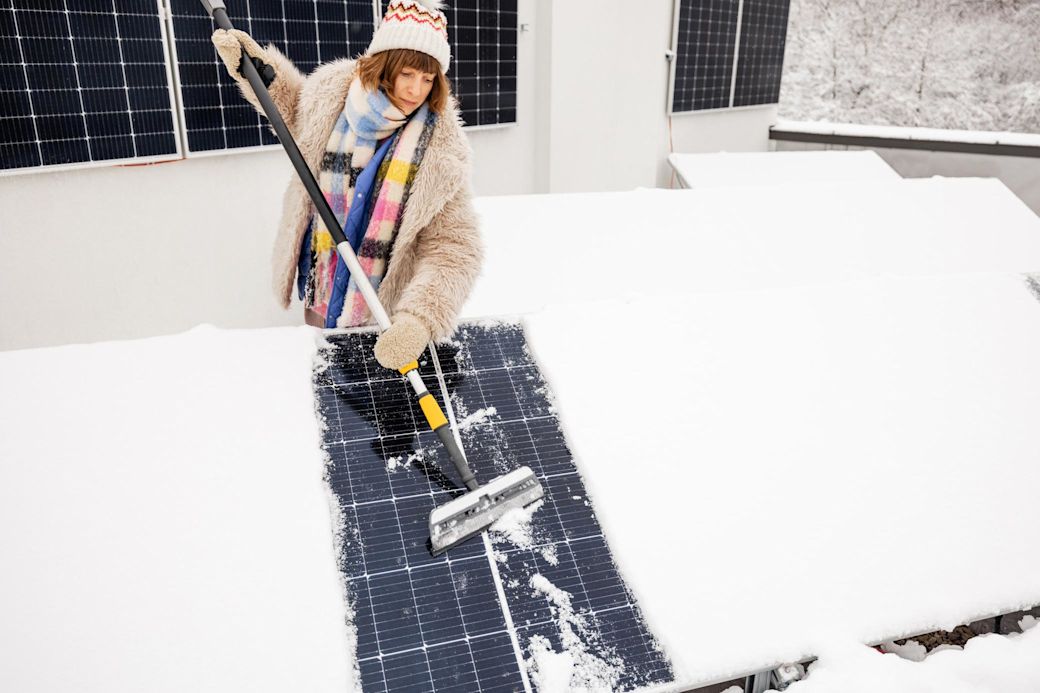 Solaranlage erzeugen auch im Winter Strom Frau befreit Solaranlage auf Dach von Schnee