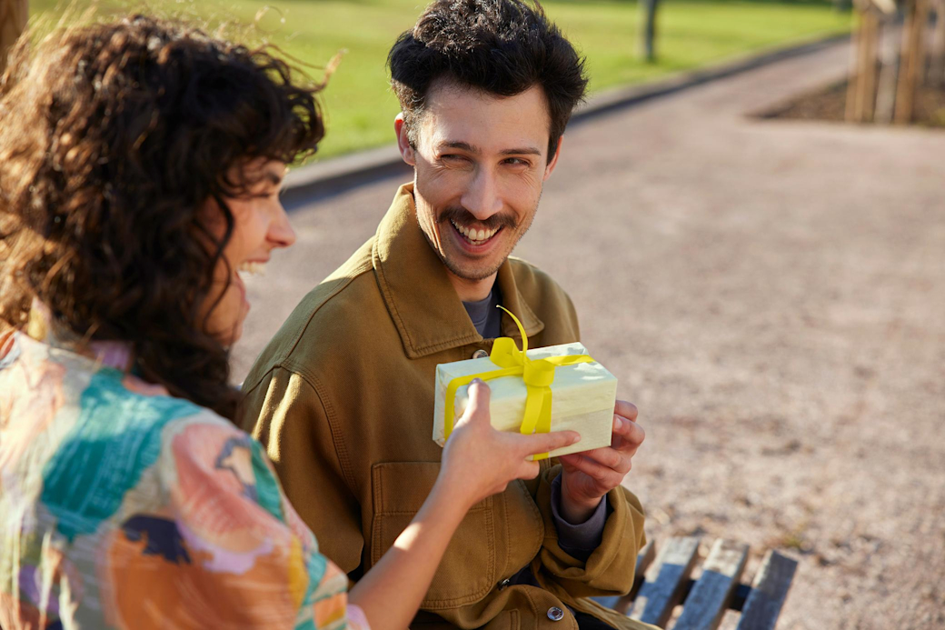 Mit dem Kombitarif von Yello erhältst du 50 € Prämie extra Frau und Mann sitzen auf einer Parkbank mit Geschenk