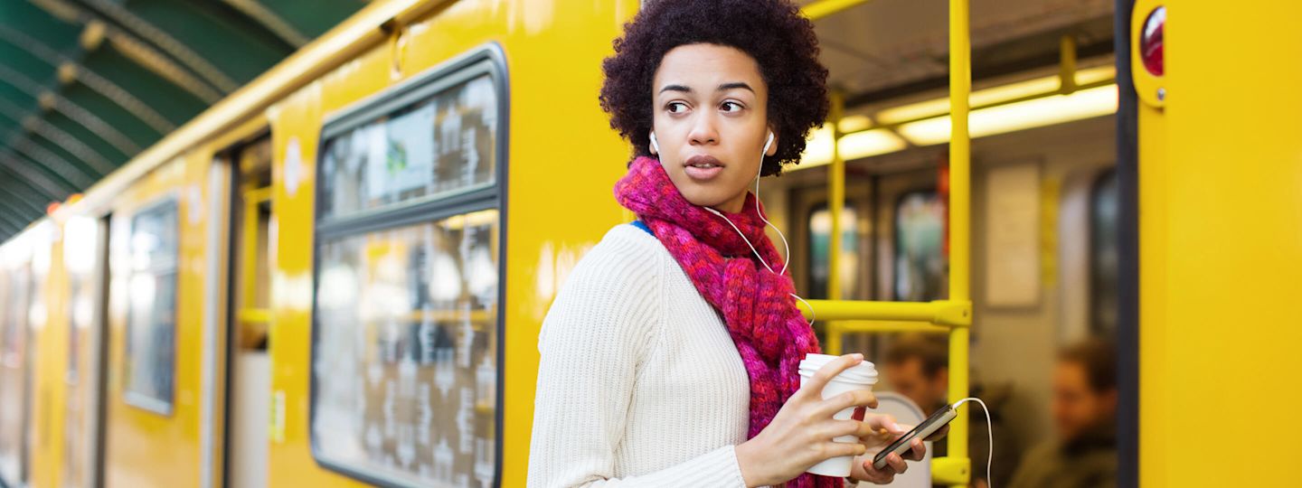 Faire Strompreise in Berlin bei Stromanbieter Yello Frau mit Smartphone und Kopfhörern steigt in Berliner Straßenbahn