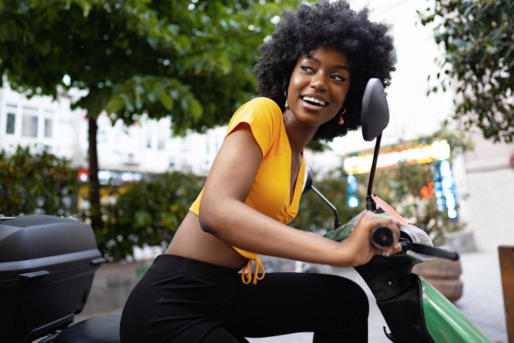 Mit dem E-Roller geht es leise und sauber durch die Stadt Frau im gelben Shirt fährt auf E-Roller durch die Stadt