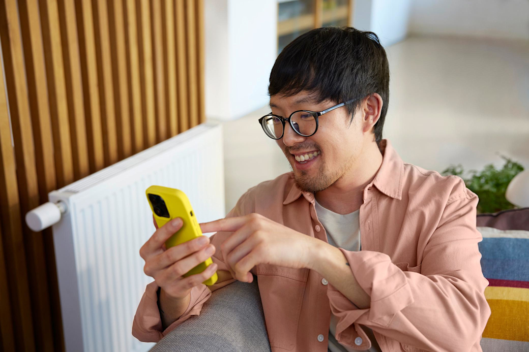 Mit Gas oder Wärmestrom heizt du dein Zuhause smart Mann auf der Couch vor der Heizung schaut aufs Handy