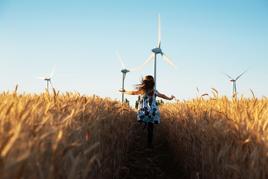 Die Energiewende ist zentral für eine nachhaltige Zukunft.  Kleines Mädchen läuft durch ein Kornfeld mit Windenergieanlagen