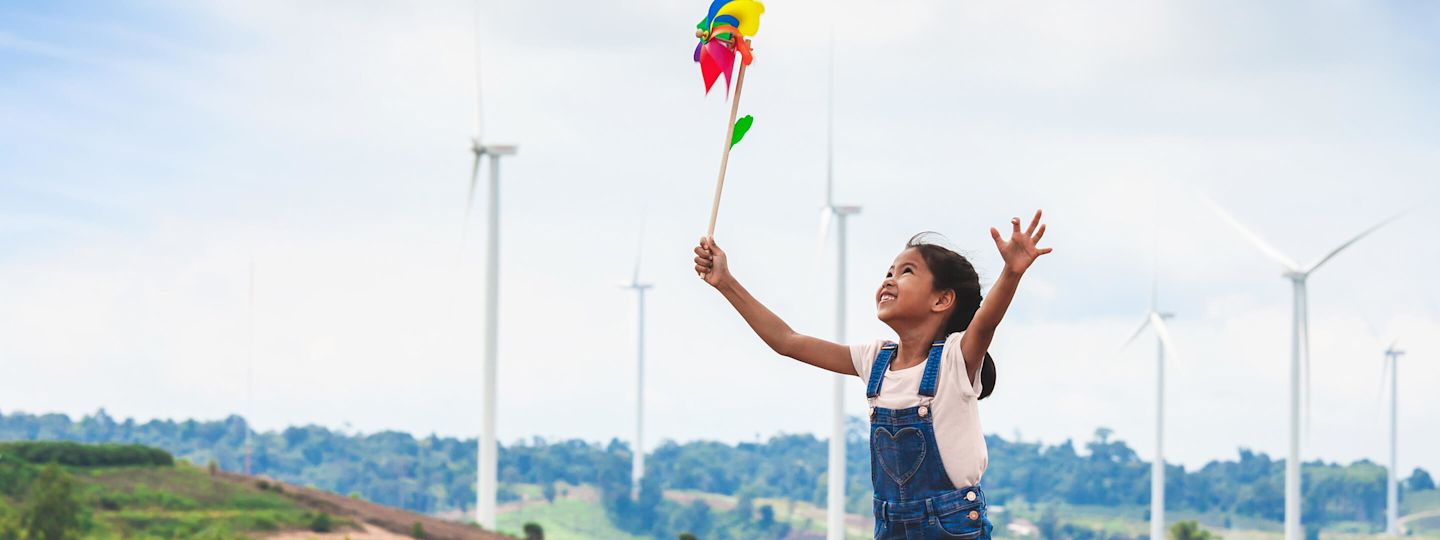 Mehr als grüne Energie: Energiewende einfach erklärt. Mädchen läuft mit buntem Windrad durch einen Windpark