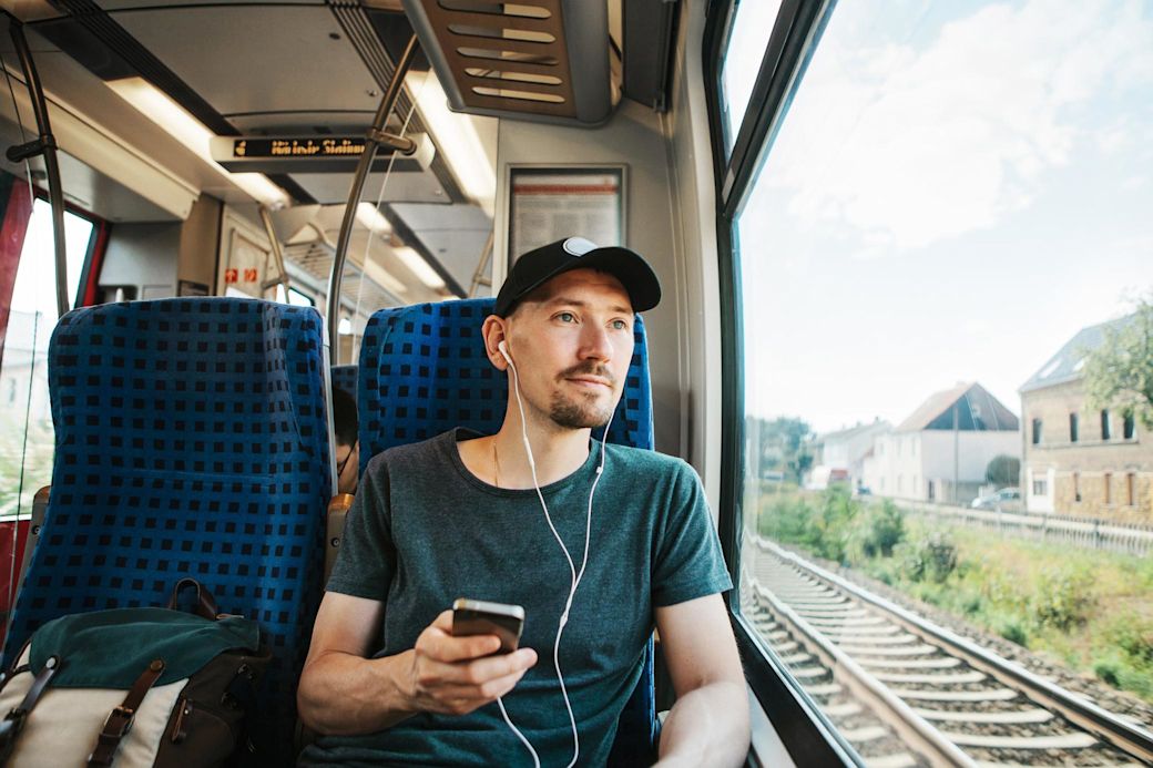 Mit nachhaltiger Mobilität kannst du CO2 und Kosten sparen Junger Mann mit Kappy und Handy fährt im Zug