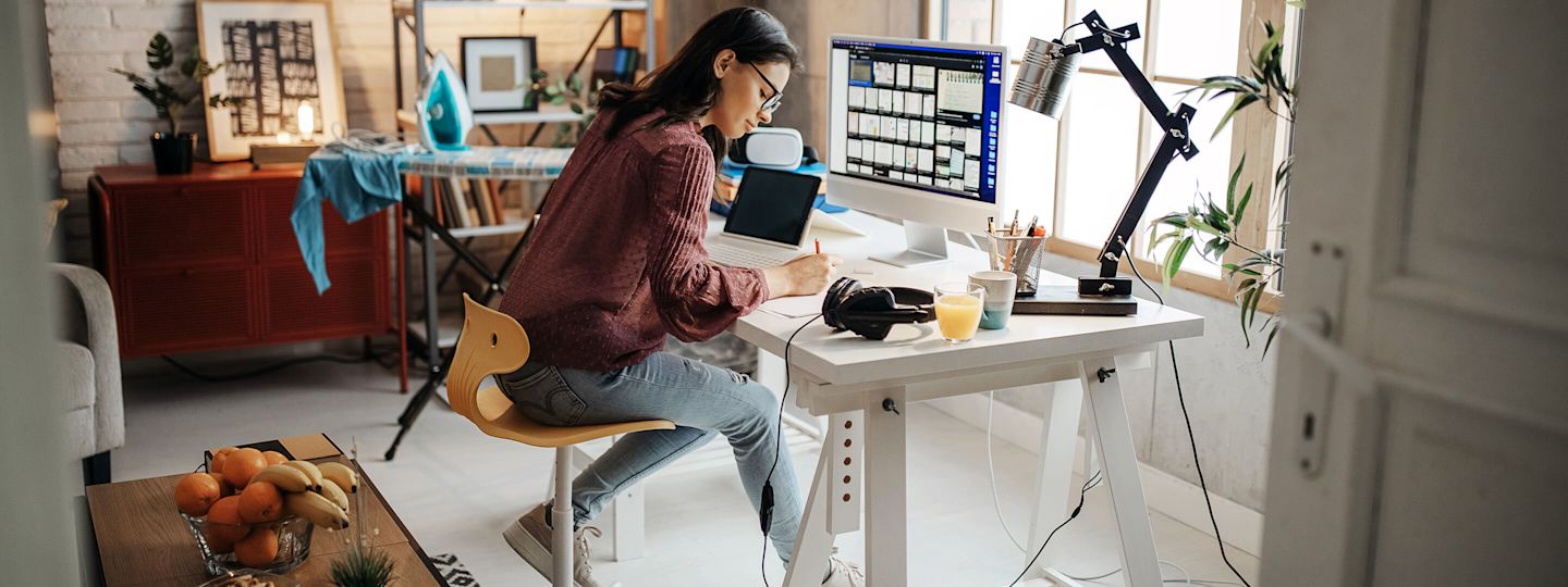 Laptop, Monitor, Lampe, Bügeleisen. Alles braucht Strom. Aber welchen? Junge Frau arbeitet zuhause am Schreibtisch.
