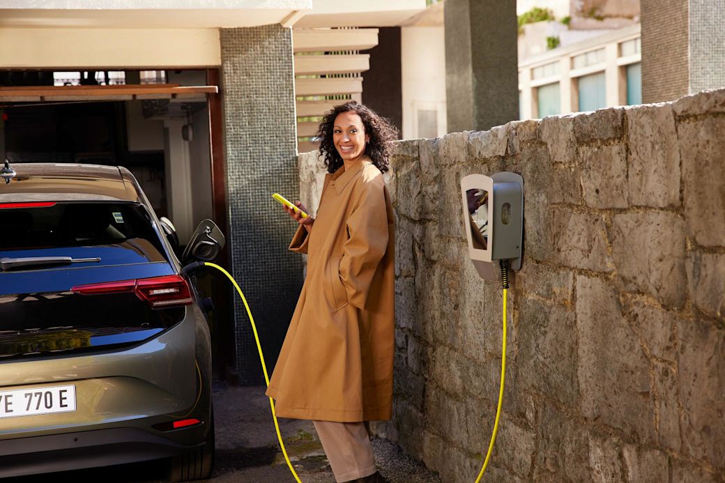 Wallbox für dein Zuhause kaufen - Das gibt's zu beachten Frau lehnt an der Wand und lädt E-Auto über eine Wallbox